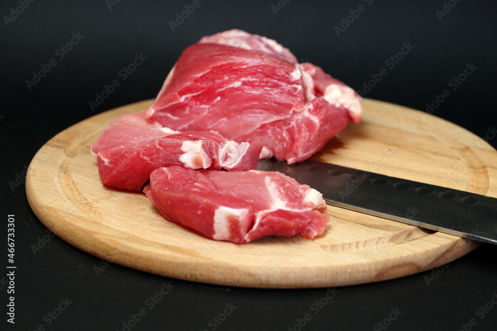 raw pork meat, knife on a round wooden cutting board on black background raw pork meat, knife on a round wooden cutting board on black background