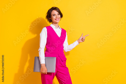 Portrait of attractive cheerful girl holding laptop showing copy empty blank space isolated over bright yellow color background