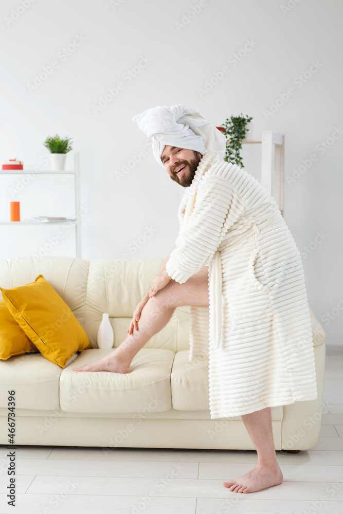 Funny portrait of handsome beautiful guy in towel and bathrobe holding tube of body cream lotion in hand. Spa, body and skin care for man concept