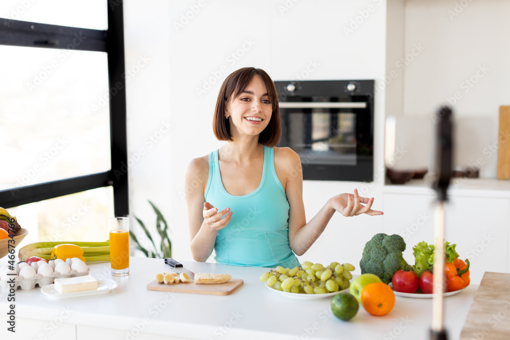 Food blogger concept. Millennial woman recording new video recipe on smartphone, standing in modern kitchen interior