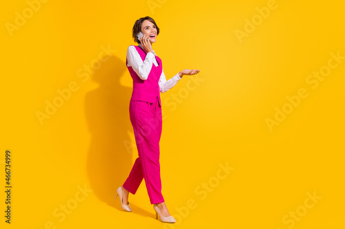 Full body photo of nice millennial brunette lady go talk telephone wear pink suit stilettos isolated on yellow background © deagreez