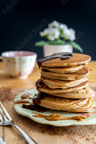 Healthy buckwheat pancake stack with chocolate, maple syrup and halvah spread on a decorative plate. Easy to make gluten free morning breakfast or brunch. Delicious heap of golden pancakes with teacup
