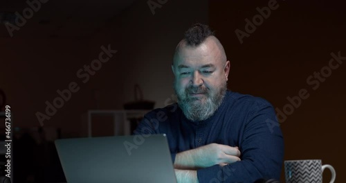 An adult bearded man cries while watching a movie on a laptop, blows his nose into a handkerchief and throws it behind his back. Accelerated video. Funny moment.