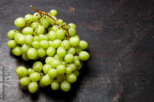 Branch of ripe green grape with water drops. Juicy grapes on wooden background, closeup. Grapes on dark kitchen table with copy space
