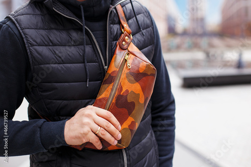 A cropped beyond recognition man holding his new brown leather banana bag in the city. Men's Leather Hip Bag Over the Shoulder Waist Bag made of genuine leather.