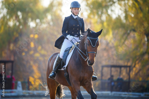 Teenage girl riding horse on equestrian dressage test in autumn.