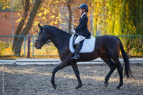 Teenage girl riding horse on equestrian dressage test in autumn. © skumer
