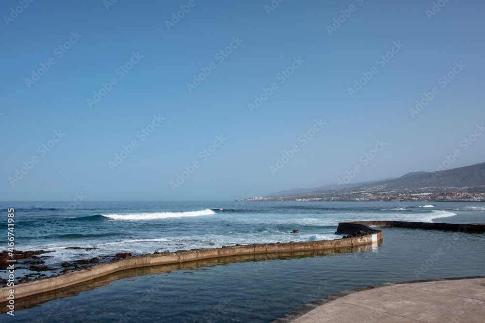 Beautiful morning with views to the ocean sporadicly filling in with salty water a nearby man-made swimming pool and ample Costa Adeje in the background, Las Americas, Tenerife, Canary Islands, Spain