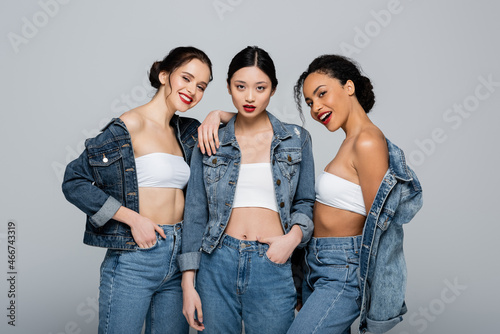 Canvas Print Smiling interracial women in denim jackets looking at camera isolated on grey