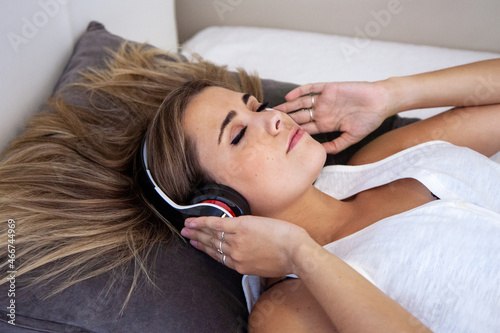 Konstfotografi Mujer escuchando música con auriculares tumbada en la cama de su habitación