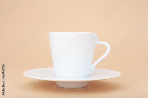 Close up of white ceramic coffee cup with saucer against pastel beige background with copy space