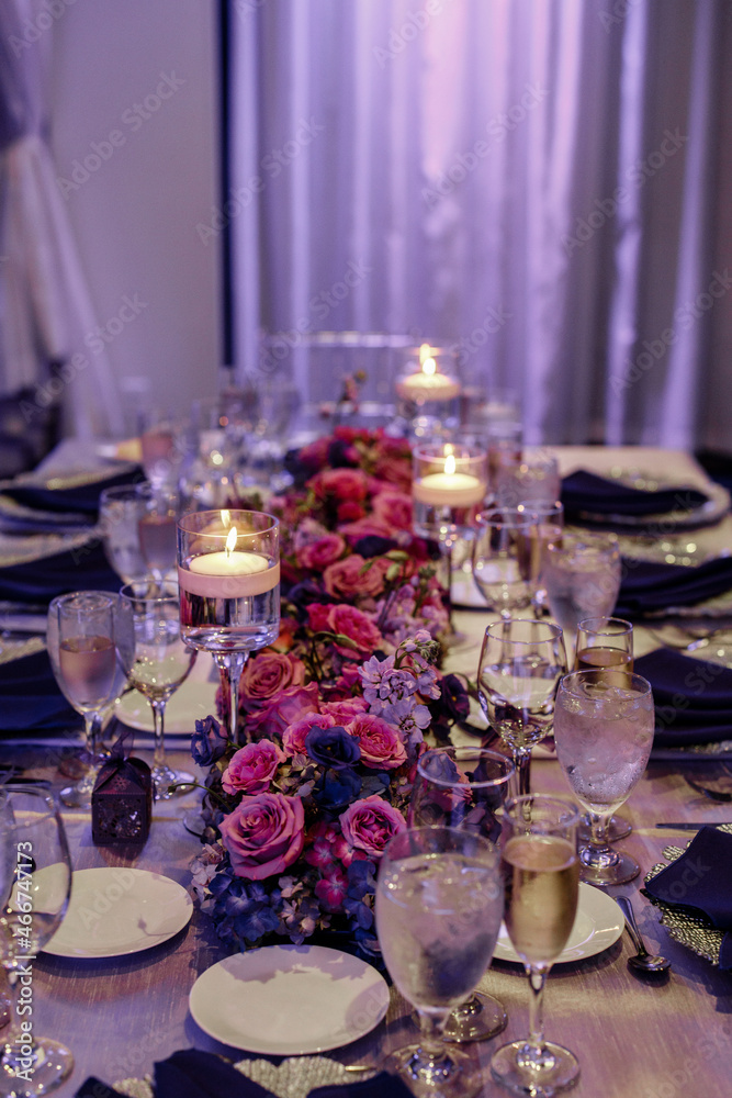 Beautiful table set with candles and flowers for a festive event party or wedding reception Candles in glass holders with liquid on wooden table Pink and violet roses table decoration floating candles