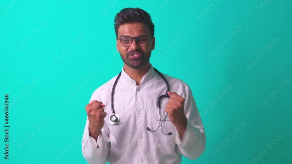 indian bearded cardiologist man with eyes glasses in white medical coat with stethoscope in blue studio background telling a good news indian bearded cardiologist man with eyes glasses in white medical coat with stethoscope in blue studio background telling a good news