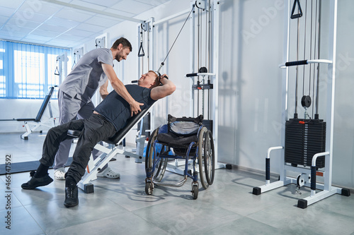 Man with disability doing exercise on strength machine with therapist