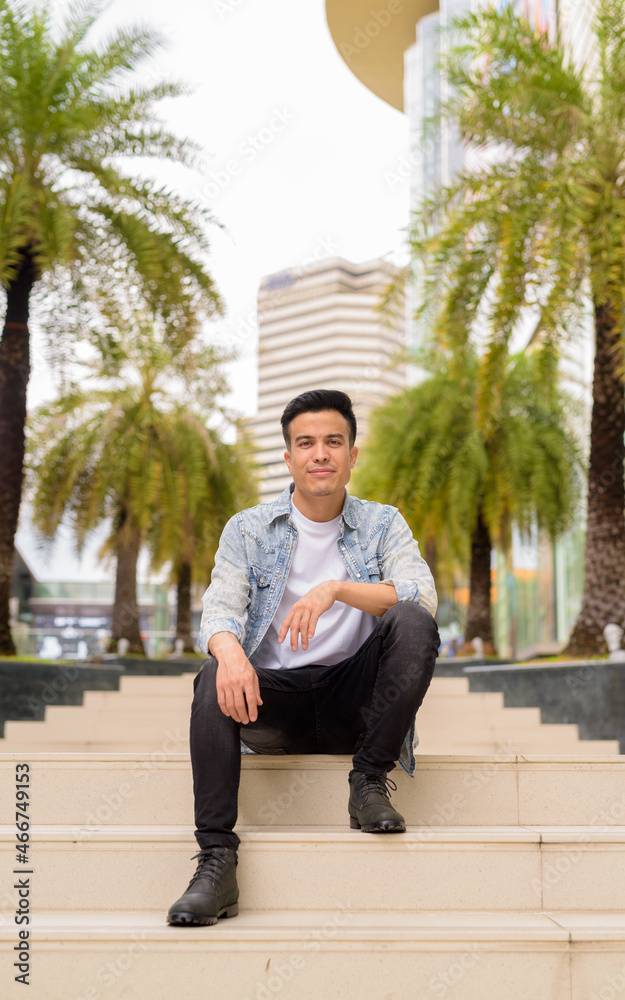 Full length portrait of handsome young man sitting outdoors in city during summer Full length portrait of handsome young man sitting outdoors in city during summer