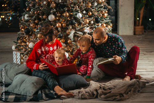 Christmas night, the family reads a book to children near the Christmas tree © Irina Flamingo