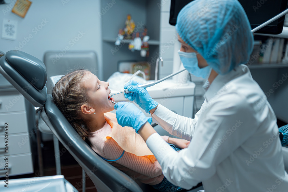 Side view of Female dentist who treats teeth of little girl patient. Dentistry concept 