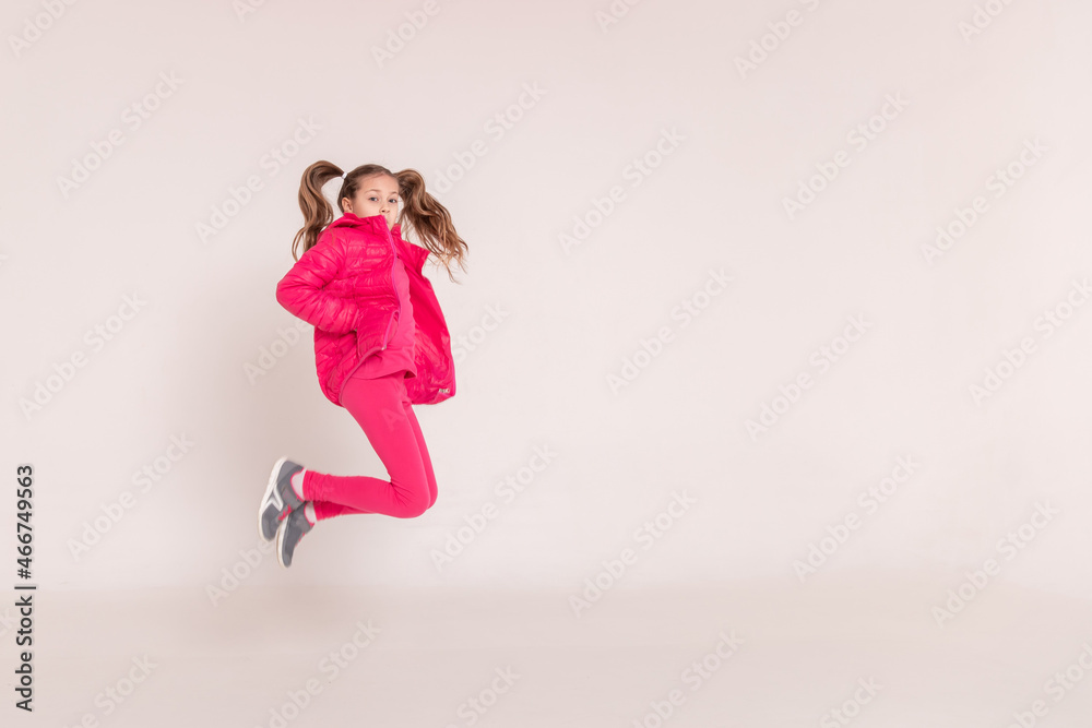 a beautiful girl in a pink jacket jumps and smiles on a white background. happy childhood.