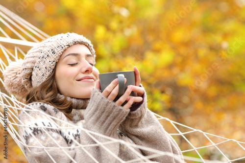 Happy woman holding coffee mug lying on hammock in autumn