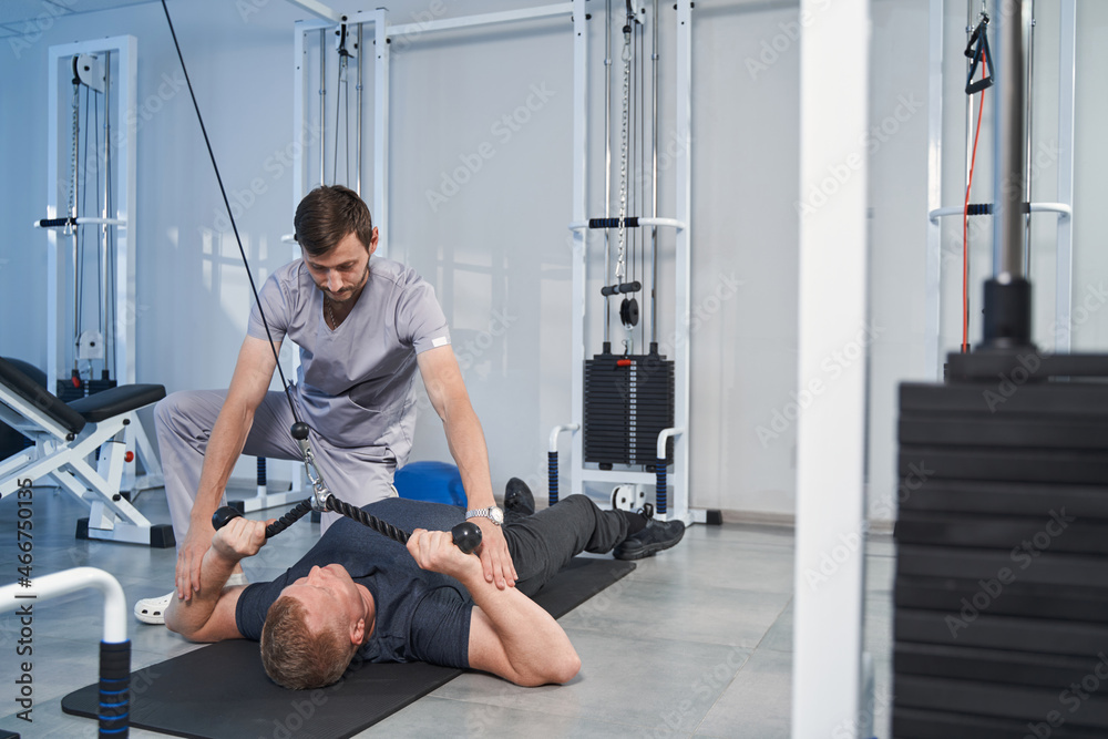 Fototapeta premium Patient with disability training on cable simulator with doctor