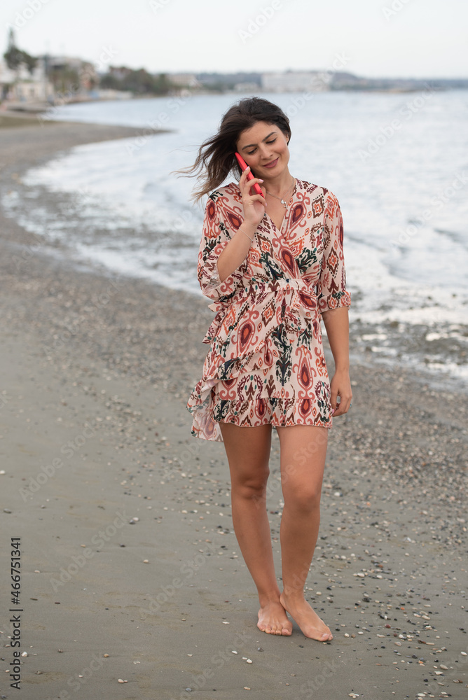 Smiling young brunette caucasian woman chatting on a red mobile phone in the beach. People lifestyle concept Smiling young brunette caucasian woman chatting on a red mobile phone in the beach. People lifestyle concept
