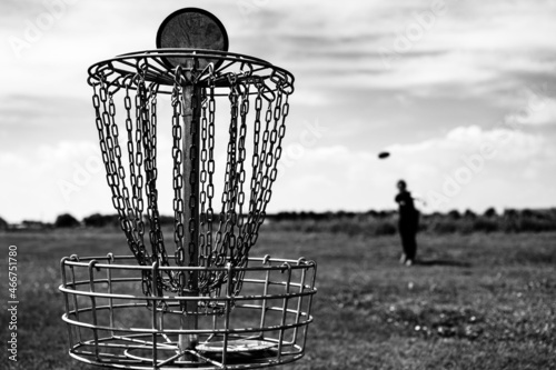 Focus on a golf hole while disc is in the air after being tossed by a defocused player