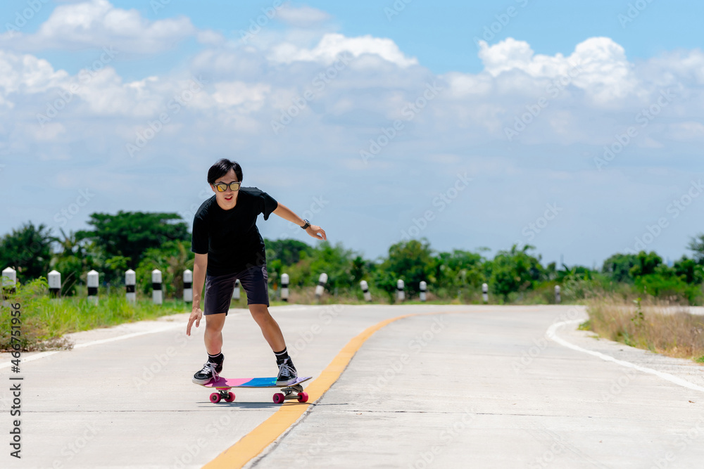 A young Asian man is wearing a black shirt and pants. play skateboard Show the posture of a turn around. On a country road on a sunny day with sky. Looking at the camera, Play surf skate.