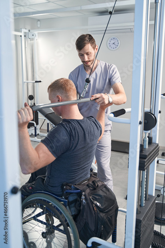 Doctor help wheelchair patient on weight machine in physiotherapy room