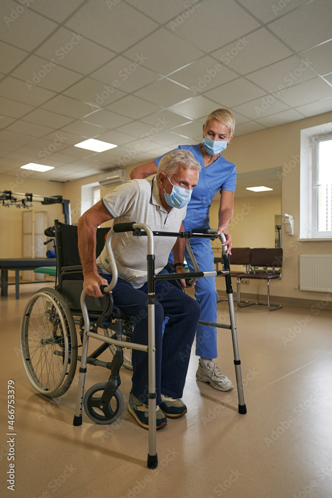 Shot of mature man walking with assistance of walker in rehab center Shot of mature man walking with assistance of walker in rehab center