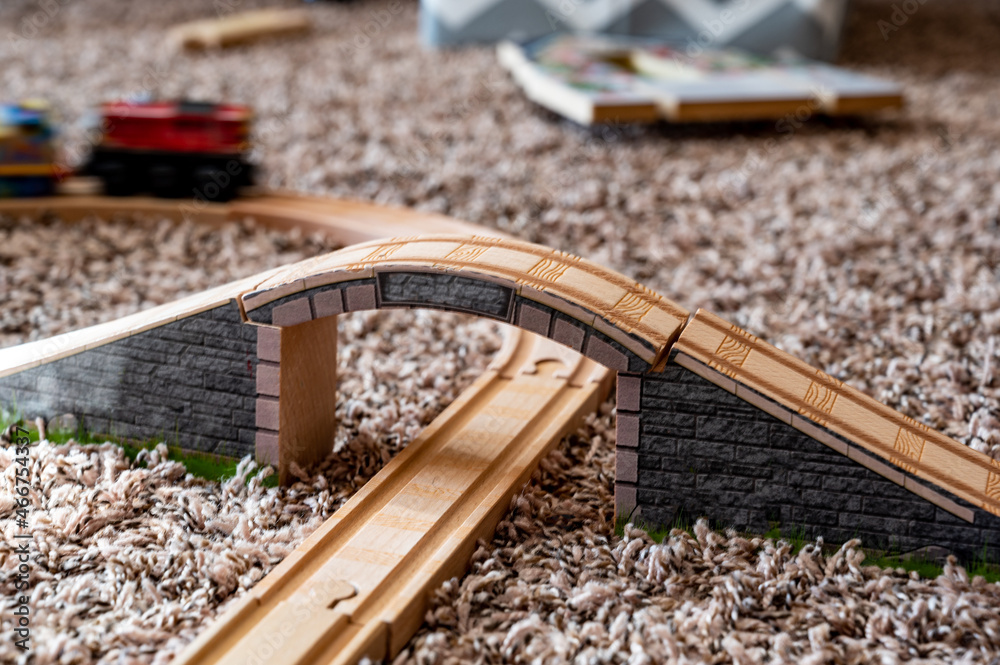 selective focus on wooden toy train track with blurred bridge and moving locomotive in background