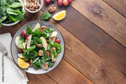 Healthy spinach salad made with red apple, wallnuts, grapes. Wooden rustic background, top view