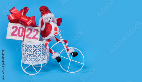 2022 text on gift box with red ribborn and santa claus toy on bicycle. Blue background. Christmas and New Year gift delivery concept. Greeting card. photo
