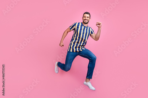 Full size profile photo of funky young brunet guy run wear t-shirt jeans sneakers isolated on pink background