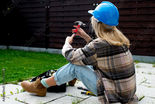 Woman in a helmet with tools. A blond woman is building a house. Female worker. Destroying gender stereotypes. Woman using different male work tools. Gender equality. woman at the construction site