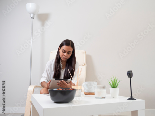 Young woman at home tired from work with a tablet sitting on a chair with a table in front of her in a relaxed atmosphere and drinking tea