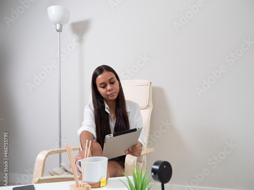 Young woman at home tired from work with a tablet sitting on a chair with a table in front of her in a relaxed atmosphere and drinking tea