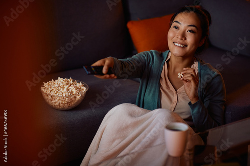 Cuadro en lienzo Happy Asian woman eats popcorn while watching TV at home at night