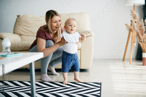 Happy mother assists her small son in taking first steps at home. photo