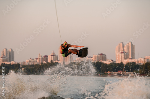healthy muscular man jumping high with wakeboard on city background.