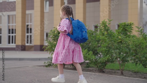 little cheerful girl runs school with backpack on her shoulders, happy kid is in hurry to first lesson, baby will receive primary preschool education, child will gain new knowledge in the classroom