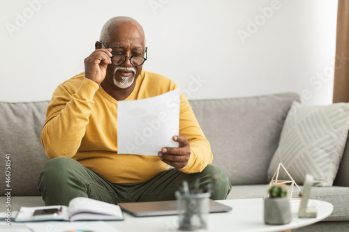 Senior African Male Working With Papers Wearing Eyeglasses Sitting Indoor photo