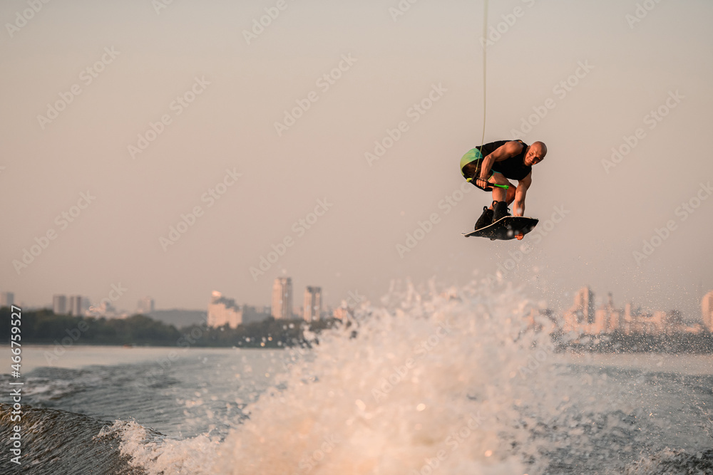 awesome view of a muscular man with a wakeboard while jumping over the wave