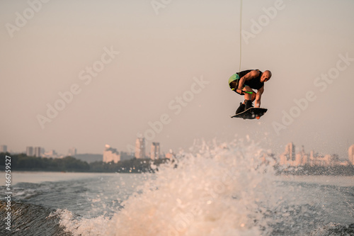 awesome view of a muscular man with a wakeboard while jumping over the wave photo