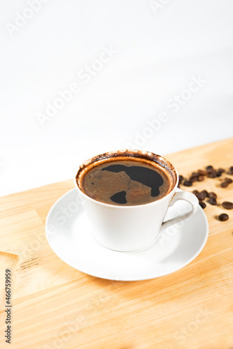 a cup of black coffee on the wooden table with some coffee beans around.  enjoying a morning coffee aesthetically.