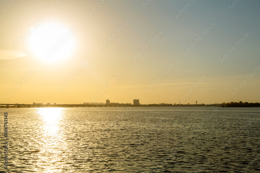 A wide river with a city in the distance at sunset.