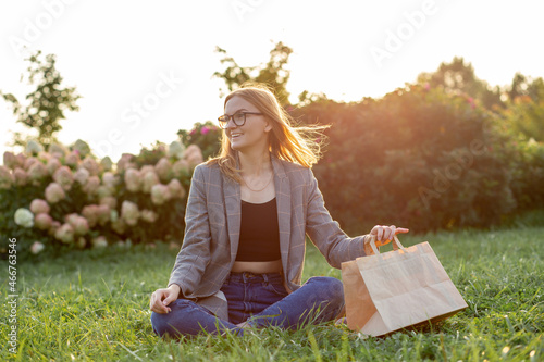 Hungy Caucasian businesswoman, student or freelancer with craft paper bag siting in the park, ordering takeaway food delivery. Concept of rest and break on job. photo