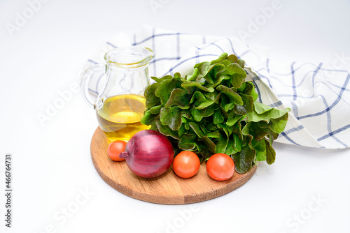 a bunch of green salad, tomatoes, olive oil, ed onion on the wooden board on white background. Ingridients for salad.