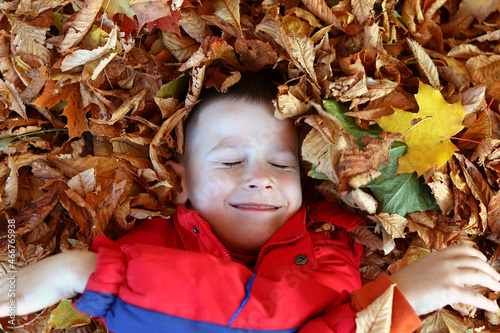 The child is lying and smiling in yellow leaves  autumn mood