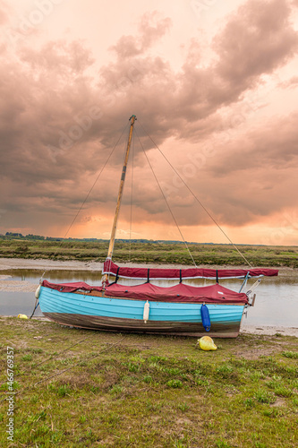 A sailing dinghy beside the River Glaven on the salt marshes at Blakeney National Nature Reserve at Blakeney, Norfolk UK
