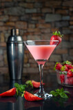 cocktail glass with a shot of strawberries and natural strawberries, metal shaker, forming a splash on black table and stone wall